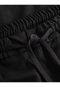 Schwarze Stoffshorts mit einem gerafften elastischen Bund, einem Kordelzugverschluss und einem seitlichen Knopfdetail. Glatte Textur mit schlichter Optik.