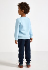 Lichtblauwe sweatshirt met geribbelde manchetten en rand, gecombineerd met marineblauwe sweatpants. Bruine sneakers met tealaccenten en beige veters.