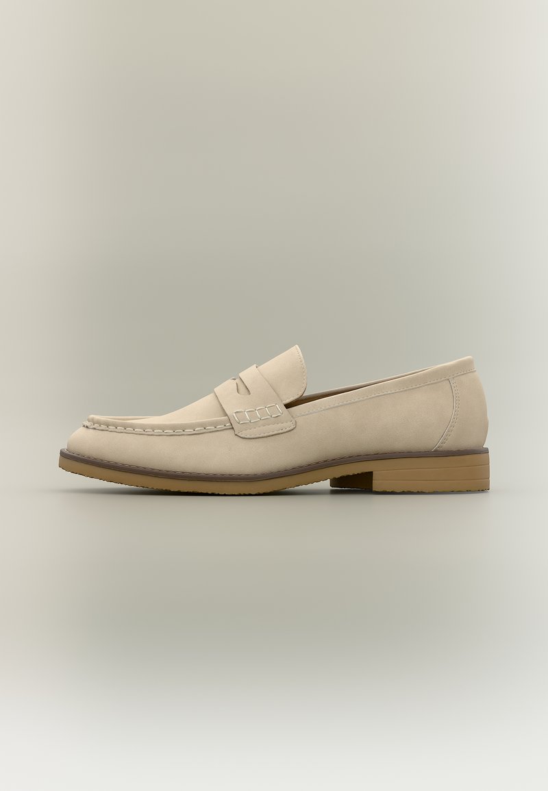 Mocassin en cuir beige clair avec un petit talon, coutures moc toe, et un détail de bride sur le dessus, présenté en profil latéral.