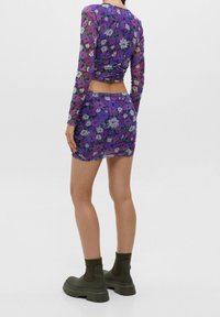 Conjunto de dos piezas floral púrpura que incluye una blusa de manga larga con fruncidos y una falda a juego. Combinado con botas de tobillo verde oliva.