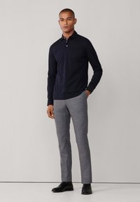 Mornarska polo majica dugih rukava s ovratnikom i tri gumba, u kombinaciji s srebrnim krojenim hlačama i crnim kožnim cipelama.