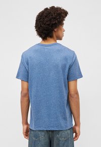 Sinine heather-tüüpi puuvillane T-särk lühikeste varrukatega ja ümmarguse kaelusega, millel on lõdva lõikega ja ühesugune värvi tekstuur taga.