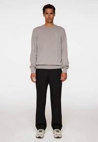 Grå stickad sweatshirt med rund hals och långa ärmar, kombinerad med svarta byxor med raka ben och vita sneakers.