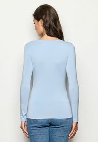 Langärmliges hellblaues Oberteil aus weichem Stoff, mit Rundhalsausschnitt und taillierter Silhouette, kombiniert mit blauen Jeans.