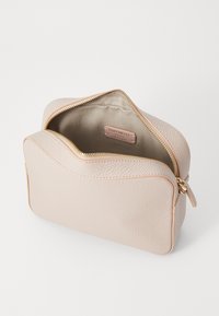 Borsa in pelle beige con una texture liscia e bordi arrotondati, dotata di una zip dorata e un'etichetta interna. Aperta per mostrare lo spazio interno.
