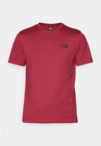 Camiseta de algodón roja con cuello redondo y mangas cortas. Presenta un pequeño logo negro en la zona izquierda del pecho. Textura suave.
