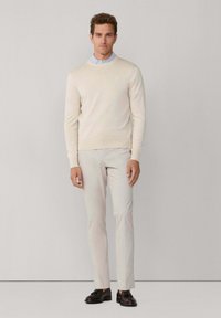 Pull beige clair avec un col rond, associé à un pantalon gris clair, coupe ajustée, et des chaussures foncées. Texture lisse, design minimaliste.