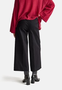 Červený, volný svetr s širokými rukávy v kombinaci s černými kalhotami s širokými nohavicemi a černými kotníčkovými botami na podpatku, které vytvářejí elegantní, moderní vzhled.