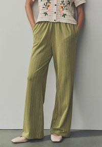 Pantalons larges verts à rayures verticales en tissu texturé. Associés à un haut en crochet avec broderies florales et détails de boutons.