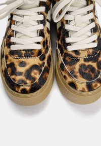 Sneaker con stampa leopardata, con parte superiore in pelliccia testurizzata, lacci color crema e una spessa suola in gomma traslucida. Punta rotonda e dettagli cuciti.