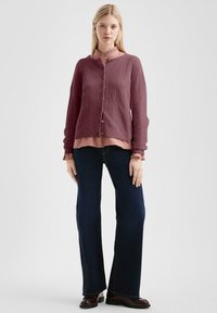 Mauve'owy kardigan z dzianiny o ryżowym tekście i zapięciem na guziki, nałożony na różową bluzkę z falbanami, zestawiony z ciemnoniebieskimi dzwonami.