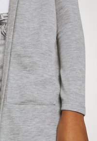 Jasnoszary kardigan, z teksturowanej dzianiny, z okrągłym dekoltem i podwiniętymi rękawami. Posiada przednią kieszeń po lewej stronie.