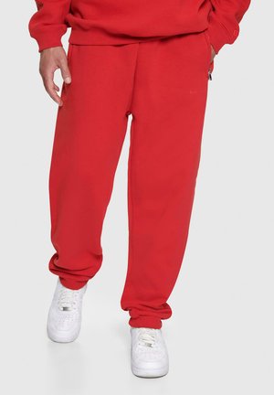 Red sweatpants with elastic cuffs and side pockets, made of soft fabric. Paired with white sneakers, featuring a classic design.