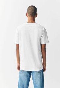 Vit kortärmad t-shirt med rund halsringning, tillverkad av mjukt tyg, med en enkel baksida och avslappnad passform. Matchad med ljusblå jeans.
