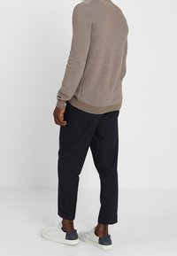 Hellbrauner Strickpullover, marineblaue cropped Hose und weiße Sneaker mit grauen Akzenten. Texturiertes Material und lockere Passform.