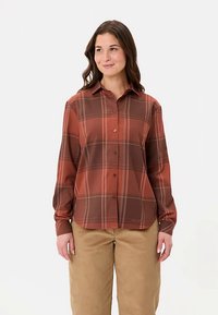 Braunes kariertes Hemd mit langen Ärmeln, durchgeknöpfter Vorderseite und Kragen. Hergestellt aus glattem Stoff mit weißen Akzentstreifen, kombiniert mit beigen Hosen.