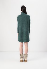 Robe en tricot à manches longues de couleur vert foncé avec un col montant. Associée à des bottes d'hiver beige avec des accents en fourrure. Design simple et décontracté.