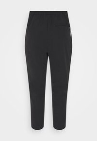 Pantalon noir fuselé avec une taille élastique et une poche zippée sur le côté droit à l’arrière, présenté sur un fond uni.