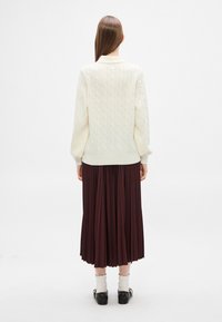 Sweter dziany w kolorze kości słoniowej z wzorem warkocza, zestawiony z bordową plisowaną spódnicą. Stylizowany z czarnymi butami i białymi skarpetkami z falbanką.