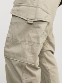 Pantaloni cargo bej, cu multiple buzunare și cusături întărite, fabricati dintr-un material durabil, cu o suprafață netedă și texturată.