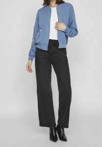 Light blue bomber jacket with a zip front, black high-waisted straight-leg jeans, and black heeled ankle boots. Smooth fabric texture.