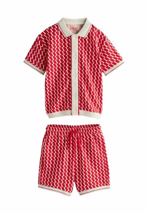 Koszula dziecięca z krótkim rękawem na guziki oraz szorty z elastycznym pasem w czerwono-biały wzór geometryczny z białym obszyciem.