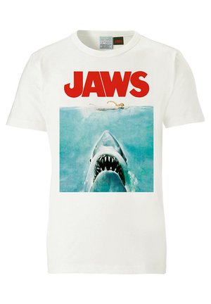 Witte katoenen T-shirt met een haai-graphic en zichtbare tanden, vergezeld van de vetgedrukte rode tekst "JAWS" boven het beeld.