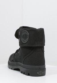 Bottines noires en toile avec un patch logo rond, semelle en caoutchouc et sangle réglable. Présente un tissu texturé et des coutures renforcées.