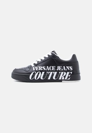Must madala säärega toss, millel on valged paelad, valge sisevooder ja külje peal suur valge tekst "VERSACE JEANS COUTURE".