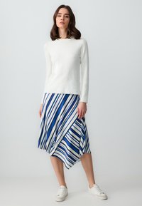 Un haut blanc à manches longues et col rond associé à une jupe rayée bleu et blanc avec un ourlet asymétrique et une texture plissée. Des baskets blanches.