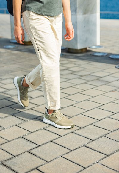 Lehké sneakers ve olivově zelené barvě s síťovaným svrškem a polstrovanou bílou podrážkou, doplněné krémově zbarvenými, mírně vyhrnutými kalhotami.