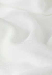 Tejido blanco con una textura suave, mostrando variaciones sutiles y un patrón de punto fino y suave. La superficie parece ligeramente brillante.