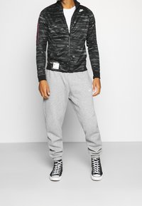 Svart zip-up jacka med ett strukturerat mönster, tillsammans med ljusgrå sweatpants. Svarta hög-top sneakers fulländar outfiten.