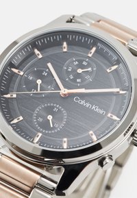 Reloj Calvin Klein con un dial texturizado negro, acentos en oro rosa, tres subdiales y una pulsera de acero inoxidable con eslabones pulidos.