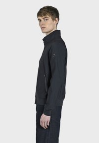 Veste zippée noire avec un col montant, dot�ée de poches latérales zippées et de poignet côtelé, faite en tissu léger et lisse.