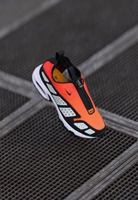 Nike-sneaker med en klar oransje overdel med svarte aksenter, hvite perforerte seksjoner og en svart såle. Slip-on-design med en pull-tab.
