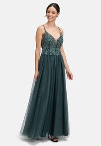 Długa, ciemnozielona suknia z dopasowaną górą, zdobiona misterną haftą, z głębokim dekoltem w kształcie litery V oraz warstwową spódnicą z tiulu, dającą efekt połysku.