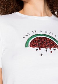 Vit bomull T-shirt med en färgglad vattenmelon-grafik gjord av röda och gröna paljetter, med svart text "ONE IN A MELON."