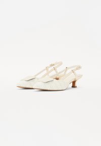 Zapatos slingback beige con tela texturizada y punta cuadrada, que cuentan con una amplia solapa frontal y un tacón bajo. Correa ajustable con hebilla.
