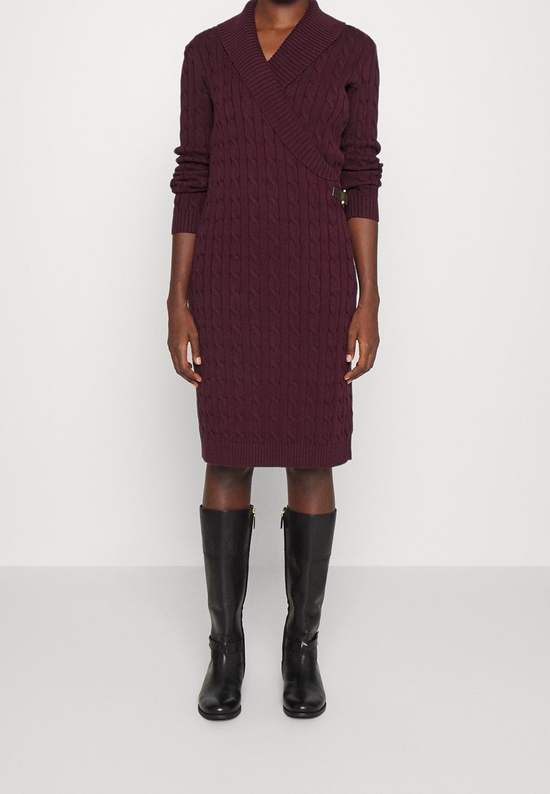 Robe portefeuille prune foncé en maille torsadée, manches longues, longueur genoux, avec un col en V, portée avec des bottes en cuir noires montant jusqu'aux genoux.