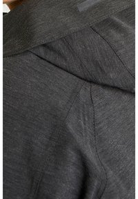 Chaqueta gris oscuro con una tela texturada, costuras pronunciadas y un cuello doblado con un sutil detalle del logo en el hombro.