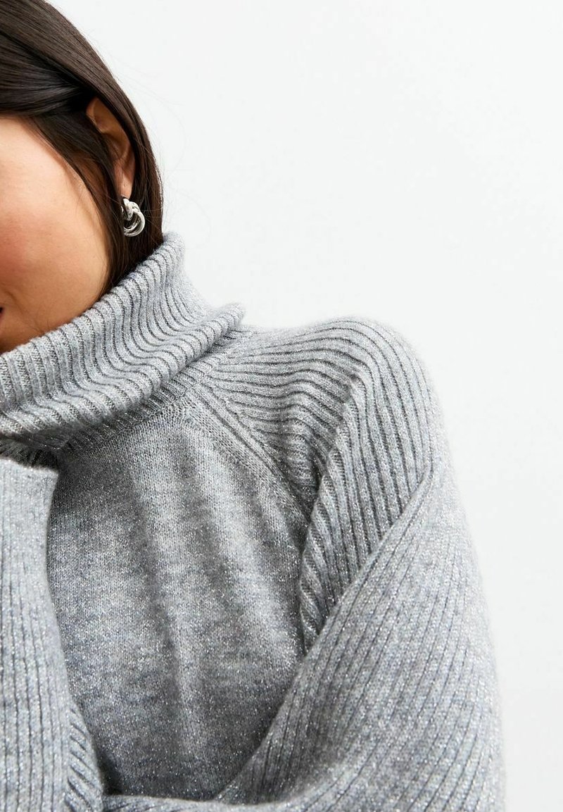 Szary sweter z golfem w prążki o miękkiej fakturze i subtelnych detalach błyszczących, podkreślający jego przytulny krój i złożony kołnierz.
