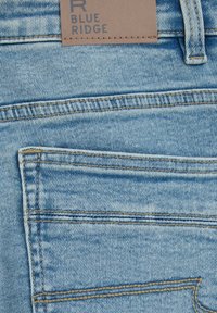 Světle modré džíny vyrobené z denimu, s zadní kapsou, kontrastním prošitím a hnědou koženou nášivkou s embosovaným nápisem "BLUE RIDGE".
