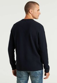 Maglione a girocollo blu navy con maniche lunghe, tessuto testurizzato e dettaglio in yoke sul retro. Abbinato a jeans in denim chiaro.