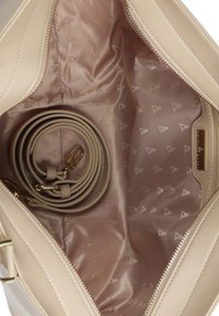 Beige håndtaskens indre har en glat, satinfinish med logo-mønster, og den har en snoet strop samt guldfarvede hardware-detaljer. Lynlåslukningen er synlig.