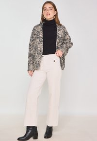 Gebreide cardigan in zwart en crème met een textuurpatroon, gedragen over een zwarte turtleneck en gecombineerd met crème corduroy broeken en zwarte enkel laarzen.