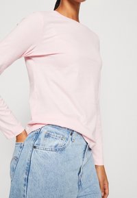 Helles, rosa Langarmshirt aus weichem Stoff, kombiniert mit hellblauen hohen Jeans. Schlichtes Design mit Rundhalsausschnitt.