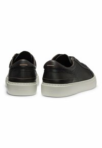Black leather sneakers with white rubber soles, featuring minimalist design, curved shapes, and subtle horizontal accents on the heel.