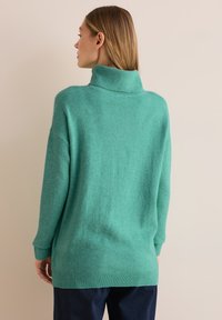 Suéter de punto oversized en turquesa con un alto cuello, textura acanalada y mangas largas. Termina a la altura de las caderas, con puños y dobladillo acanalados.