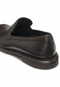 Dunkelbrauner Leder-Schlupfschuh mit strukturierter Oberfläche, abgerundetem Zehenbereich, markanter Ferse und kontrastierenden roten Steppnähten.